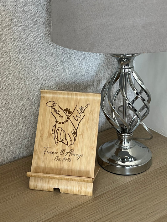 A unique personalised bamboo phone stand laser-engraved with a couple holding hands, two names & a date. Perfect wedding, anniversary or Valentine's gift.