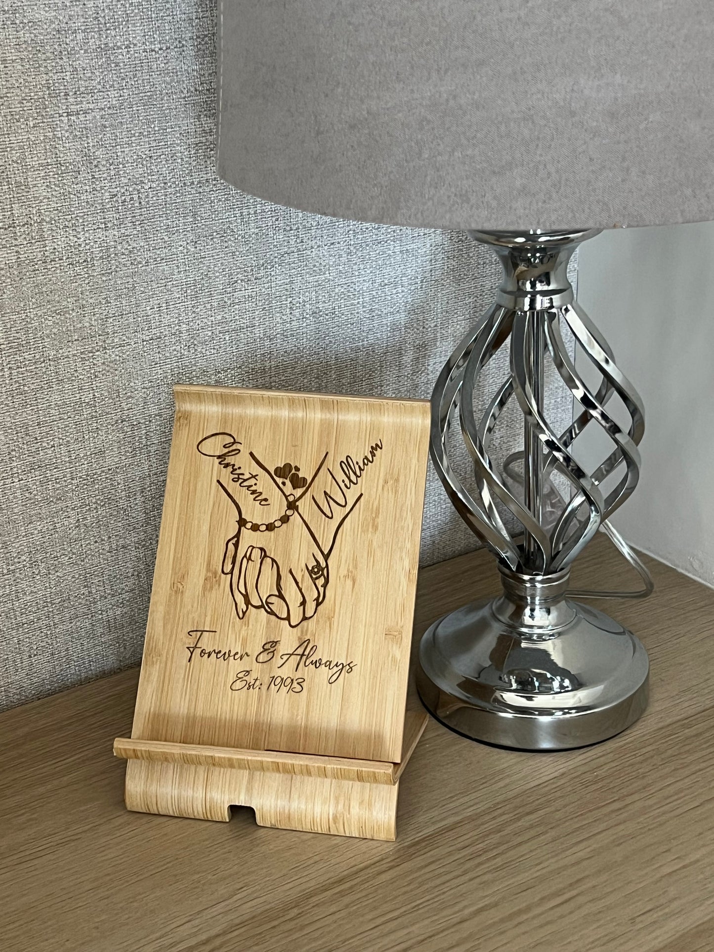 A unique personalised bamboo phone stand laser-engraved with a couple holding hands, two names & a date. Perfect wedding, anniversary or Valentine's gift.